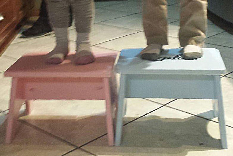 Lower Legs and Feet of Two Children Standing on Two Stools.